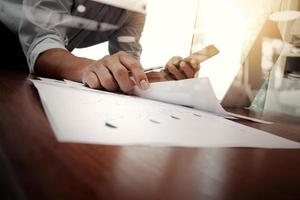 business documents on office table with smart phone and laptop computer and graph business with social network diagram and man working in the background photo