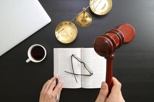 justice and law concept.Top view of Male judge hand in a courtroom with the gavel and brass scale and computer and open bible book on dark wood table photo