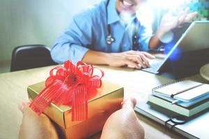 entrega de regalos. mano o equipo del paciente dando un regalo a un médico sorprendido en el consultorio del hospital, efecto de película de filtro foto