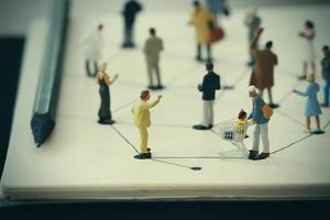 close up of miniature people with social network diagram on open notebook on wooden desk as social media concept photo