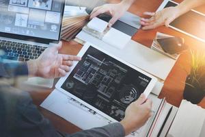 top view of two colleagues interior designers discussing data with new modern computer laptop and pro digital tablet with sample material on wooden desk as concept photo