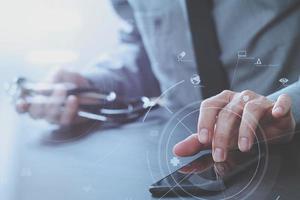 close up of smart medical doctor working with mobile phone and stethoscope on dark wooden desk with virtual reality icon diagram photo