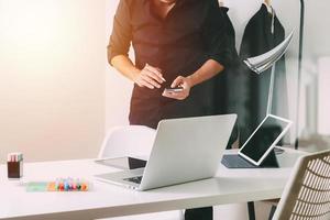 Fashion designer working with mobile phone and using laptop with digital tablet computer in modern studio photo