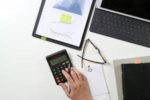 vista superior de la mano de hombre de negocios que trabaja con finanzas sobre costos y calculadora y portátil con teléfono móvil en el escritorio en la oficina moderna foto