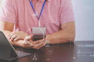 businessman in pink t-shirt working with smart phone and digitl tablet computer on wooden desk in modern office with virtual icon diagram photo