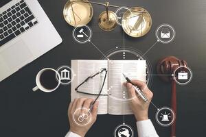 justice and law concept.Top view of Male judge hand in a courtroom with the gavel and brass scale and computer and open bible book on dark wood table with Vr diagram photo