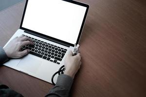 vista superior de la mano del médico que trabaja con una computadora moderna y una pantalla en blanco en un escritorio de madera como concepto médico foto