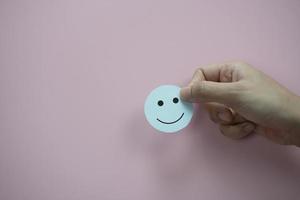 Hand holding green happy smiley face paper cut on pastel pink background photo