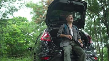 Asian Senior man, retired, sitting on a car use binoculars looking at the birds in the trees, in the woods, and writing down the information in a notebook. happily on vacation days video