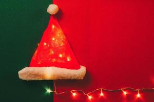 concepto de temporada de saludo sombrero de santa claus con luz de navidad sobre fondo rojo y verde foto