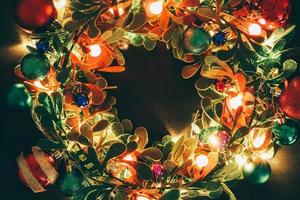 concepto de temporada de saludo corona de navidad con luz decorativa sobre fondo de madera oscura foto