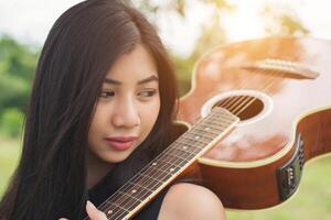 hermosa mujer sosteniendo una guitarra en su hombro, parque natural de verano afuera. foto