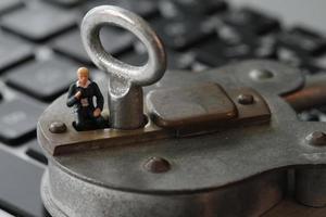 Concepto de seguridad en Internet: empresario en miniatura se para en una llave antigua y candado en el teclado de la computadora portátil