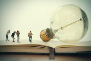 Creative idea concept - miniature photographer with vintage light bulb on open paper notebook photo