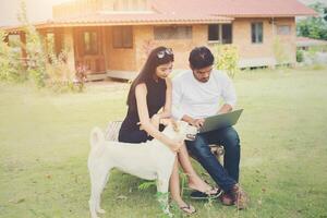 una joven pareja de educación sentada en el banco juega con un perro al aire libre y hace buen tiempo. y son felices, concepto de estilo de vida. foto