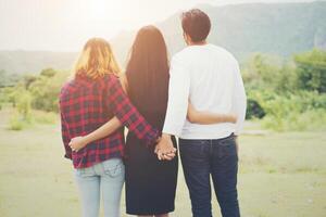 triángulo amoroso, el hombre está abrazando a una mujer y se está tomando de la mano con otra chica, de pie al aire libre en el parque. foto