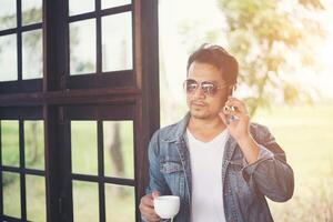 Hipster man holding a cup of coffee and walk in the coffee shop, Relaxing talking on phone. photo