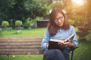 chica encantadora hipster relajándose en el parque mientras lee un libro, disfruta de la naturaleza. foto