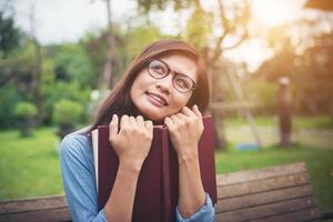 chica encantadora hipster pensando en algo mientras lee un libro rojo en el parque verde. foto