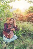 Young beautiful hipster woman hug with her guitar sitting on grass in the park, Relaxing with nature. photo