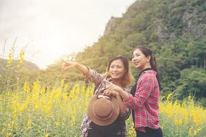 dos mujeres hipster viajando y señalando con la mano disfrutando juntas del campo de flores, relajándose un buen día soleado. foto