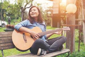 Beautiful young woman playing guitar sitting on bench, Happy time concept. photo