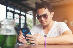 joven feliz mirando su teléfono móvil y sonriendo mientras está sentado en el café. foto