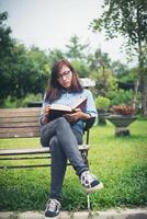 chica encantadora hipster relajándose en el parque mientras lee un libro, disfruta de la naturaleza. foto