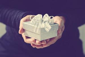 gift giving,man hand holding a gift box in a gesture of giving.blurred background,bokeh effect,vintage photo