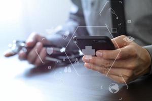 close up of smart medical doctor working with mobile phone and stethoscope on dark wooden desk with virtual reality icon diagram photo