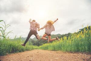 Young hipster couple in love outdoor jumping at yellow flower field with mountain sunset background. Jump up high enjoying freedom and enjoy. photo