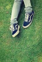 Woman's legs wearing jeans with sneaker sitting on the grass. photo