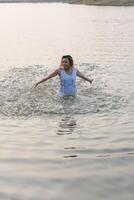 Feliz mujer hermosa con vestido blanco disfruta jugando al agua en el lago. foto