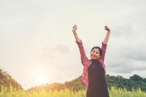 Young happy woman raising hands in yellow flower field on sunset,mountain view backgound. photo