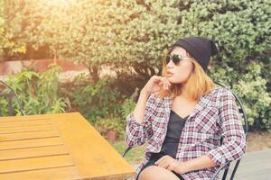 Outdoor portrait of young hipster woman sitting alone at old city cafe and waiting for her boyfriend wearing plaid outfit and  sunglasses. photo