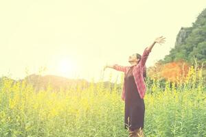 Young happy woman raising hands in yellow flower field on sunset,mountain view backgound. photo