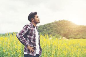 hombre hipster de pie en el campo de flores en el día de verano, disfrute de la naturaleza. foto