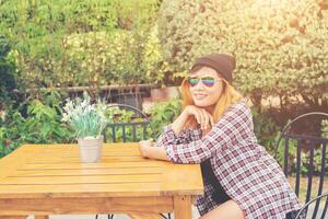 Outdoor portrait of young hipster woman sitting alone at old city cafe and waiting for her boyfriend wearing plaid outfit and  sunglasses. photo