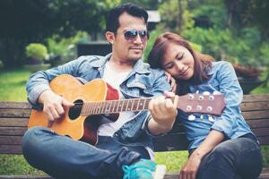 Young couple in love playing acoustic guitar in the park while sitting on the bench together. photo