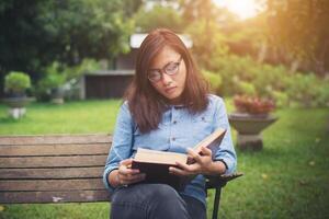 chica encantadora hipster relajándose en el parque mientras lee un libro, disfruta de la naturaleza. foto