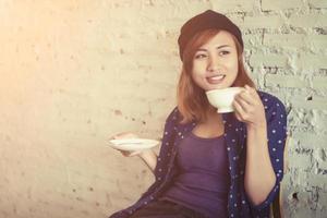 hermosa mujer con una taza de café sentada sobre un fondo de ladrillos blancos. foto