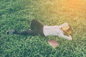 Young hipster woman lying down on grass when she tired after read book. photo