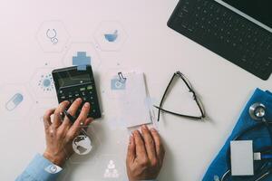 top view of Healthcare costs and fees concept.Hand of smart doctor used a calculator for medical costs in modern hospital with VR icon diagram photo