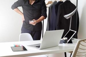 Fashion designer using mobile phone and using laptop with digital tablet computer in modern studio photo