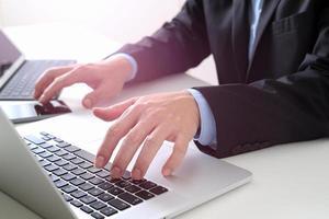Hands of businessman typing on laptop in modern office with smart phone and digital tablet computer photo