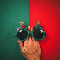 Christmas glasses that decoration with Christmas tree and red ball on hand on green and red  background photo