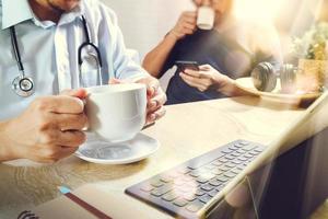 Medical doctor team taking coffee break.using digital tablet docking smart keyboard and smart phone on marble desk.listen music,filter film effect photo