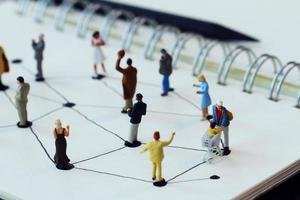 close up of miniature people with social network diagram on open notebook on wooden desk as social media concept photo