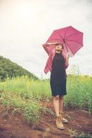 Young beautiful woman holding red umbrella in Yellow flower field and mountain background. photo