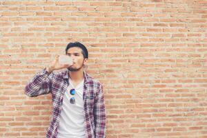 joven hipster barbudo con botella de agua en camisa a cuadros frente al fondo urbano. foto